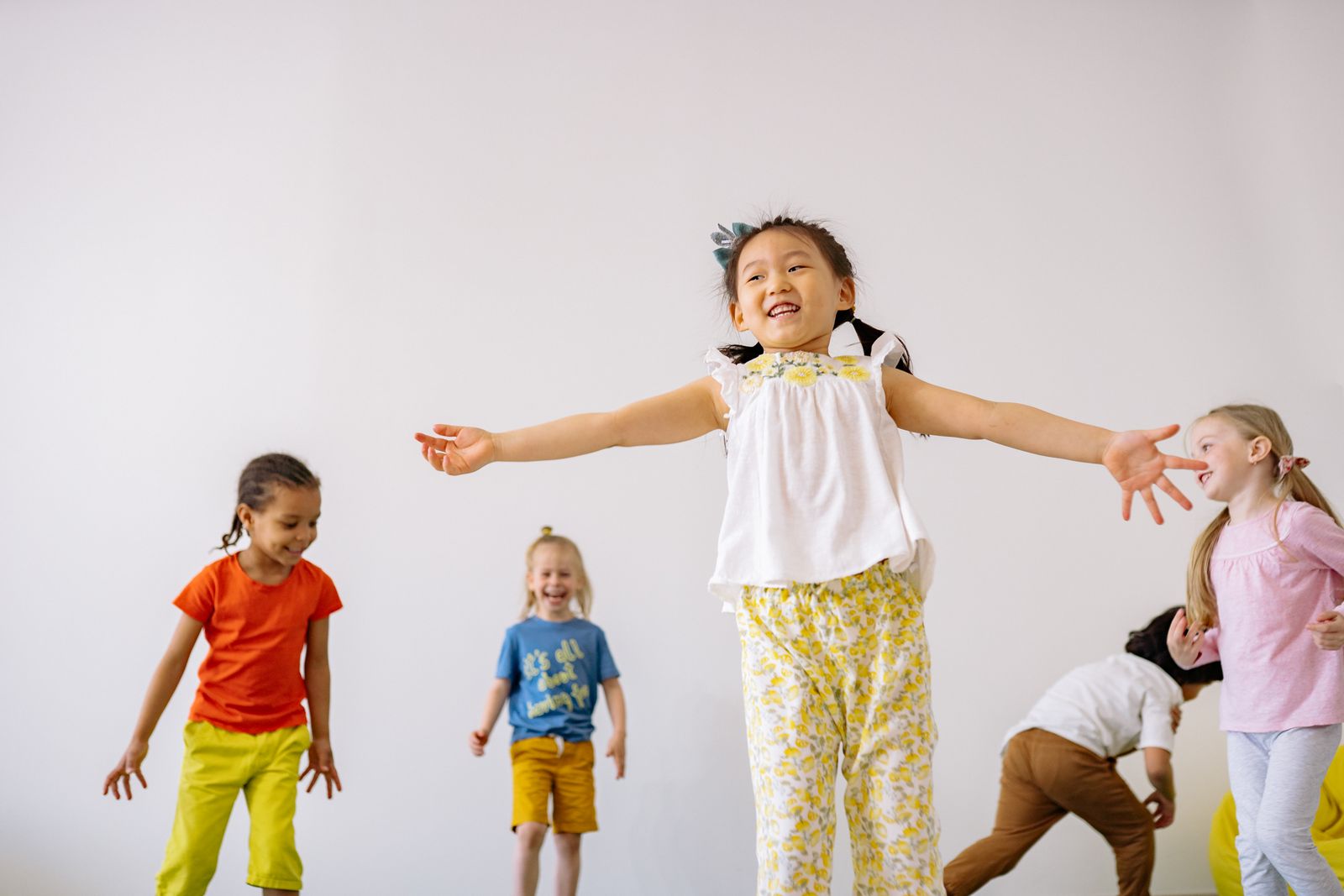 A smiling girl stretching her arms out while children move and play together